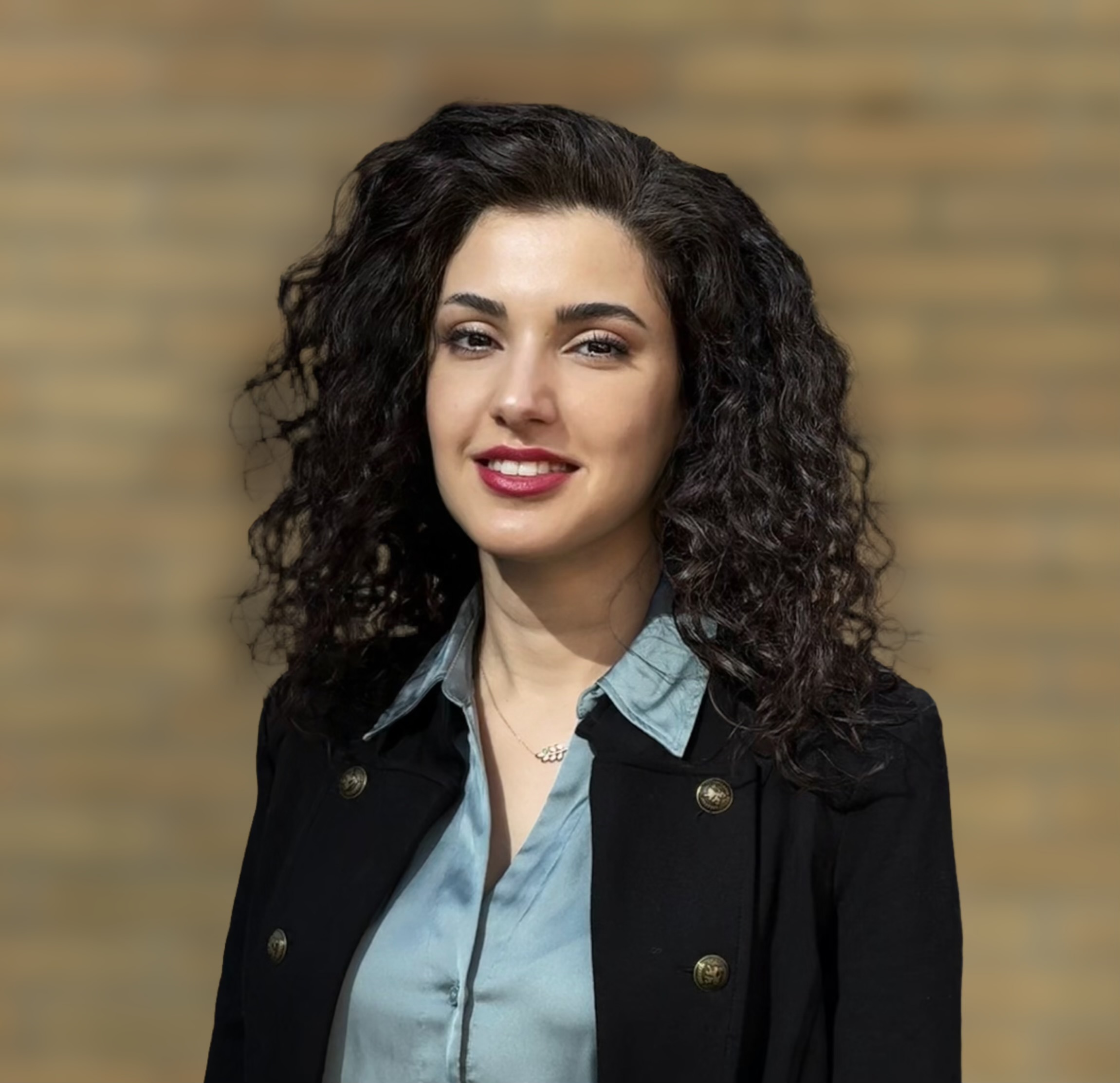 Professional headshot of Mona Hoorvash, who is wearing a blue collared shirt under a dark blazer and has shoulder-length wavy brown hair.