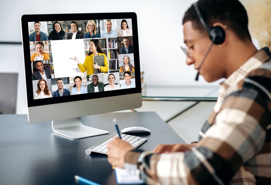 Male-presenting person with a headset on taking handwritten notes while on a virtual classroom call.