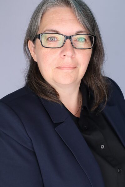 Dr. Ann Gagné wearing a black shirt inside a navy blue blazer and smiling into the camera with shoulder-length ombre hair and dark-rimmed glasses.